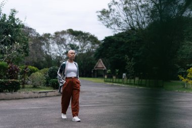 Kel Asyalı kadın dışarıda yürüyor, kendine güveni ve gücü doğal ortamında somutlaştırıyor.