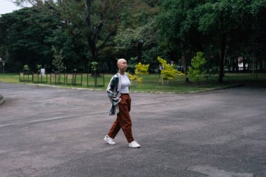 Kendine güvenen genç, kel Asyalı kadın dışarıda yürüyor, modern bireysel tarzını ve şehir yaşam tarzını ifade ediyor.