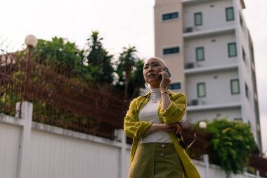 Kendine güvenen kel Asyalı kadın dışarıda akıllı telefondan konuşuyor, şehirde bağımsız bir yaşam tarzını benimsiyor.