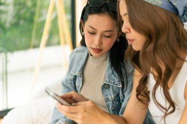 Genç Asyalı kadınlar etkileşimde, birlikte cep telefonu ekranına bakıyorlar, sosyal medya içeriğini paylaşıyorlar.