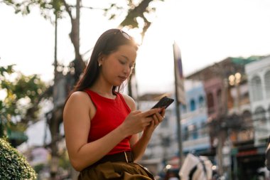 Açık havada akıllı telefon kullanan, bağlı kalan ve şehir yaşamını yönlendiren genç bir kadın.