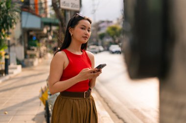 Genç Asyalı kadın dışarıda cep telefonu kullanıyor, meşgul şehir yaşam tarzıyla bağlantı kuruyor.
