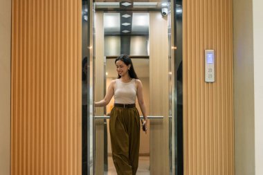 Asansörden inerken gülümseyen genç Asyalı kadın günlük rutinine başlıyor.