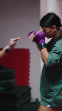 İki atletik kadın antrenmana katılıyor bir boks salonunda yumruk ve tekme pratiği yapıyorlar.