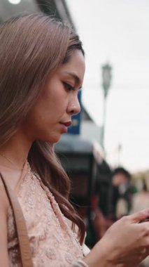 Geleneksel Tayland elbisesi giymiş genç bir kadın şehir ortamında akıllı telefonuyla konuşuyor.