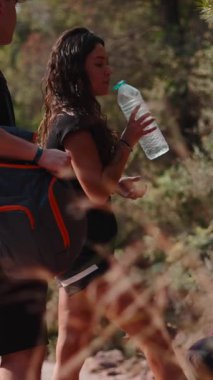 Bir grup yorgun arkadaş yürüyüş sırasında bir şişeden suyla su içiyorlar - 4K Yatay