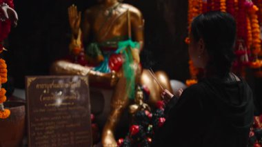 Tapınakta altın bir heykelin önünde dua ederken elinde tütsü çubukları tutan genç adam - 4K yatay