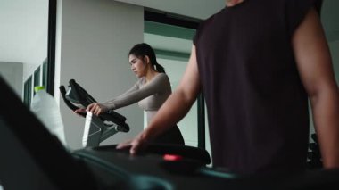 Asyalı erkek ve kadın koşu bantlarında sağlıklı bir yaşam için birlikte antrenman yapıyorlar.