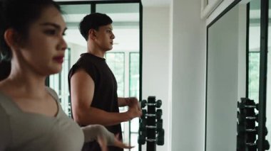 Genç Asyalı erkek ve kadın spor yapmadan önce kol sallama ve rotasyonlarıyla ısınıyorlar.