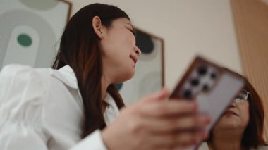 İki Asyalı iş kadını modern bir ofiste akıllı bir telefonla iş birliği yapıyor ve bir projeyi tartışıyorlar.