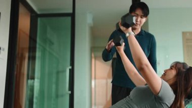 Genç Asyalı bir kadın spor salonunda erkek eğitmeniyle birlikte göğüs presi yapıyor.
