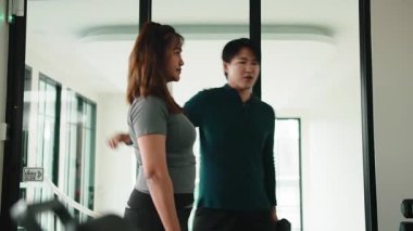 Erkek eğitmen, spor salonunda ağırlık kaldıran bir kadını çalıştırıyor.