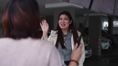 İki mutlu bayan arkadaş yağmurlu bir günde otoparkta birbirlerine sıcak bir kucaklaşmayla selam veriyorlar.