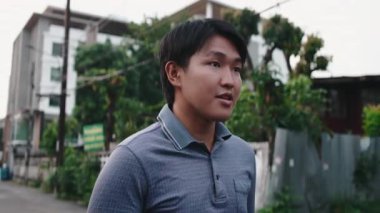 Genç Asyalı bir adam sessiz bir yerleşim yerinde birini bekliyor. Beklendiği gibi etrafa bakıyor.