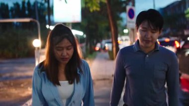 Genç ve mutlu Asyalı çift, bir randevu gecesinde şehir kaldırımında birlikte yürüyorlar.
