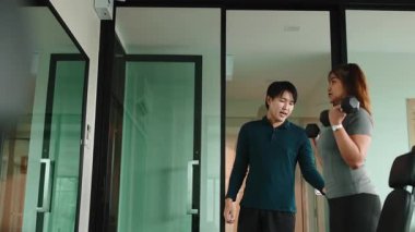 Genç Asyalı özel antrenör, modern bir spor salonunda bir kadına halter egzersizlerinde yardım ediyor.