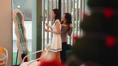 İki Asyalı genç arkadaş takılıyor, biri saçını tararken diğeri makyaj yapıyor.