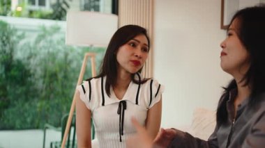 İki Asyalı kadın kanepede oturup oturma odasında samimi bir konuşma yapıyorlar.