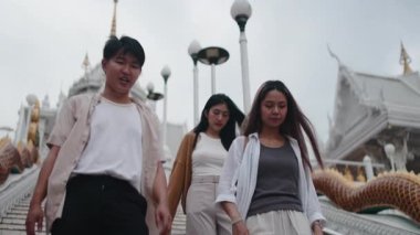 Bir grup Asyalı genç arkadaş geleneksel Tayland tapınağının merdivenlerinden birlikte iniyorlar.