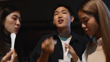 Bir grup yetişkin arkadaş Asyalı bir şehir gecesinde bir sokak satıcısından lezzetli yerel yiyecekler yiyorlar.