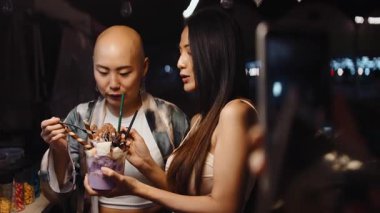 İki mutlu Asyalı kadın gece marketinde lezzetli bir dondurma yiyor.