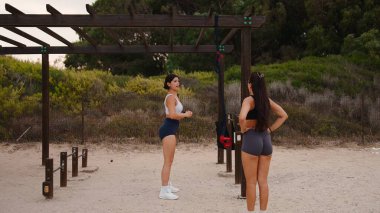 Açık hava antrenmanına çıkan iki genç kadın, ahşap bir spor salonunun yanında duruyorlar.