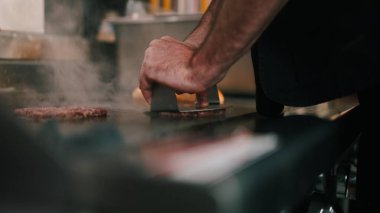Profesyonel aşçı restoranın mutfağında mangalda hamburgerleri eziyor.