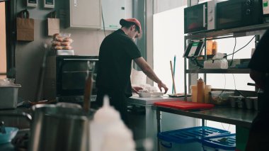 Şef karanlık bir mutfakta servis için yemek hazırlıyor, paket servis ve hayalet mutfak operasyonlarına odaklanıyor.