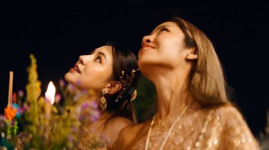 Loy Krathong şenliklerini izleyen iki Taylandlı kadın mum ve tütsü ile Krathongları serbest bırakıyorlar.