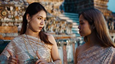 Büyüleyici geleneksel elbiseler giyen iki Taylandlı kadın antik bir tapınağın yakınında sohbet ediyorlar.