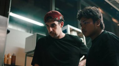 Şefler karanlık bir ticari mutfakta yemek hazırlama iş akışı üzerinde çalışıyorlar.