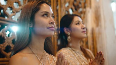 Geleneksel Tayland elbisesi giyen iki kadın Loi Krathong Festivali 'nde el ele dua ediyor.