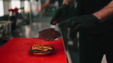 Profesyonel aşçı, restoranın mutfağında kırmızı bir kesme tahtasıyla lezzetli bir hamburger hazırlıyor.