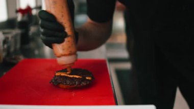Profesyonel aşçı gurme burger hazırlıyor, köfteye imzalı sos ekliyor.