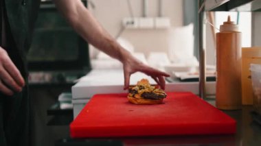 Erkek, ticari bir restoranın mutfağında lezzetli bir hamburger hazırlıyor.