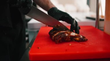 Erkek aşçı, siyah eldiven giyip restoranda kırmızı bir kesme tahtasıyla domuz pirzolası kesiyor.
