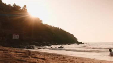 İnsanlar okyanusta yürürken ve yüzerken sakin bir tropikal plajda altın güneş ışığı parlıyor.