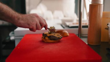 Profesyonel aşçı lezzetli bir cheeseburger hazırlıyor ve köfteye taze tat katıyor.
