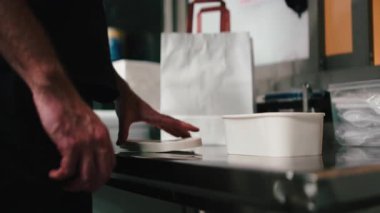 Restoran çalışanı yemek hazırlıyor, teslimat için bir konteynırı kese kağıdına koyuyor.