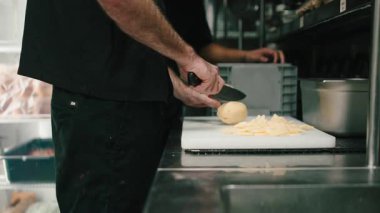 Tanımlanamayan bir şef, ticari bir mutfakta patates dilimlemek için bıçak kullanıyor.