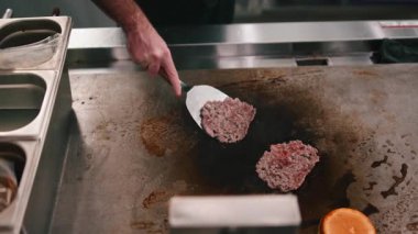 Erkek aşçı spatula kullanarak taze kıymalı köfte pişiriyor. Ticari ızgarada pişiyor.