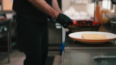 Profesyonel bir aşçı ticari bir mutfakta leziz ızgara domuz pirzolası hazırlıyor ve tabakta pişiriyor.