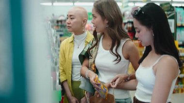 Bir markette alışveriş yaparken raftan ürün seçen üç farklı bayan arkadaş.