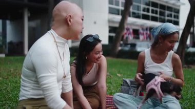 Arkadaşlar parkta dinleniyor, güneşli bir günde bir chihuahua köpeğiyle gülüyor ve oynuyorlar.