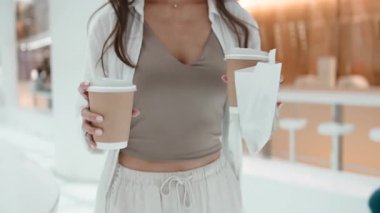 Modern bir kafede, elinde kahve fincanları ve bir kese kağıdında pasta tutan tanınmamış bir kadın.