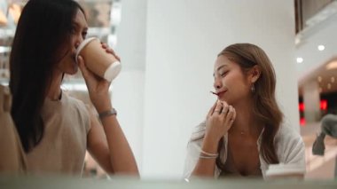 Modern bir kafede sohbet eden, gülen ve kahve içen iki Asyalı genç kadın.