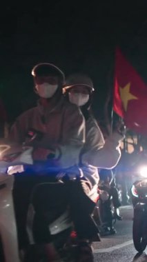 Bir futbol maçı zaferinin ardından motosiklet süren ve bayraklarını sallayan Vietnamlı bir kalabalık.