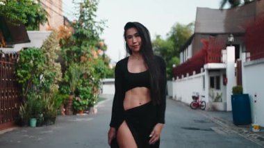 Spor kıyafetleri içindeki güzel Asyalı kadın şehrin caddesinde kameraya doğru yürüyor.