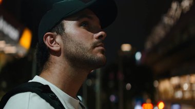 Parlak bir gece şehrini keşfeden şapkalı bir adam aydınlanmış binalara bakıyor.