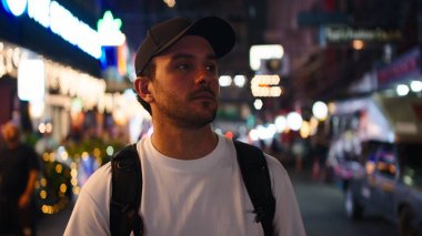 Genç adam hareketli gece hayatını izliyor, şehir ortamında yeni manzaralar keşfediyor.